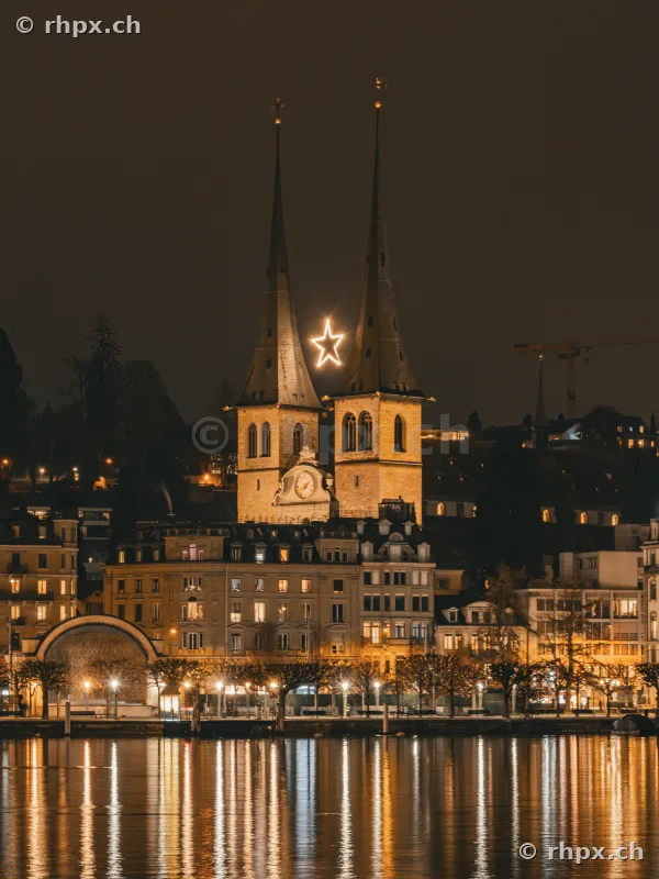 Illuminated towers of the Hofkirche in Lucerne with a glowing star between the spires at night.