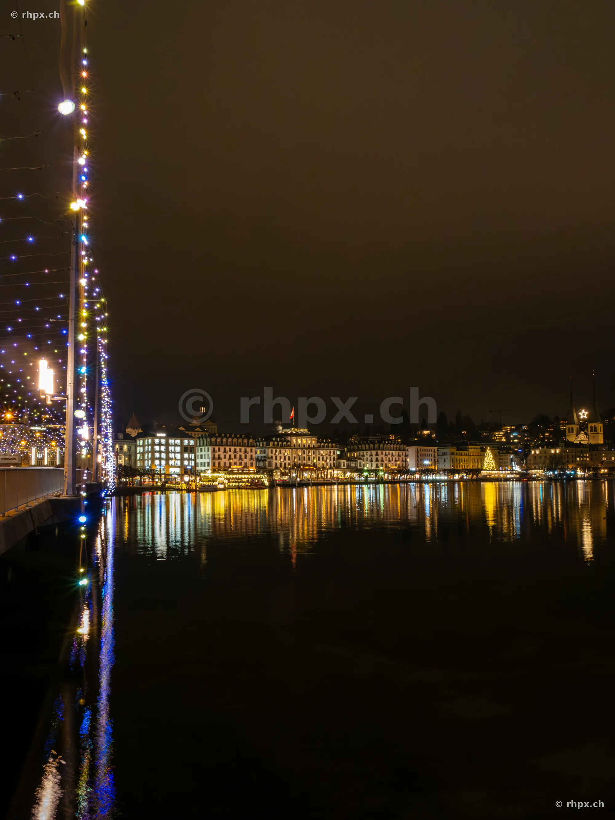 Night view of Lucerne's lakeshore promenade with festive Christmas lights and reflections in Lake Lucerne.