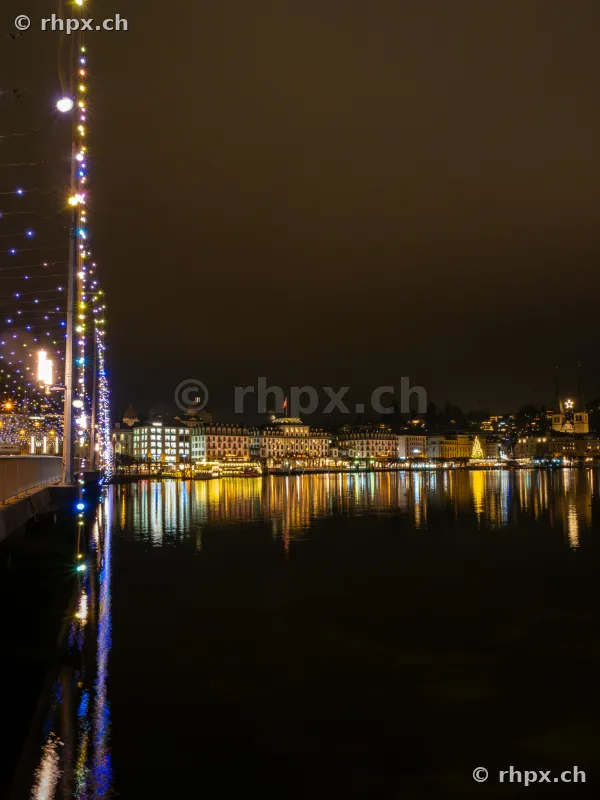 Night view of Lucerne's lakeshore promenade with festive Christmas lights and reflections in Lake Lucerne.