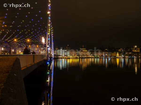 Nächtliche Seebrücke in Luzern mit bunter Weihnachtsbeleuchtung und Blick auf das beleuchtete Seeufer