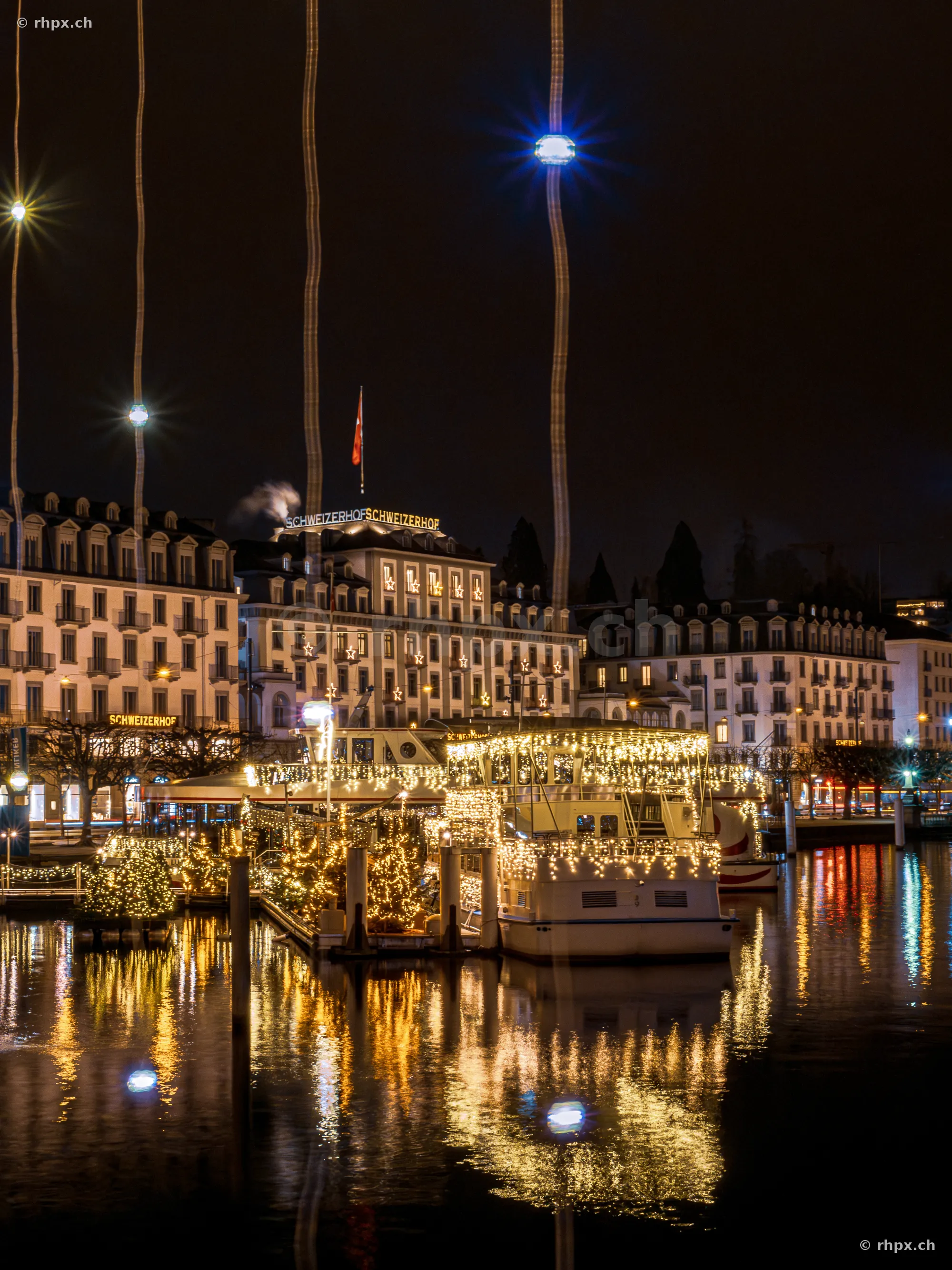 Festively lit boat at the Lucerne waterfront with Hotel Schweizerhof in the background at night