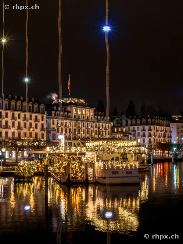 Festively lit boat at the Lucerne waterfront with Hotel Schweizerhof in the background at night