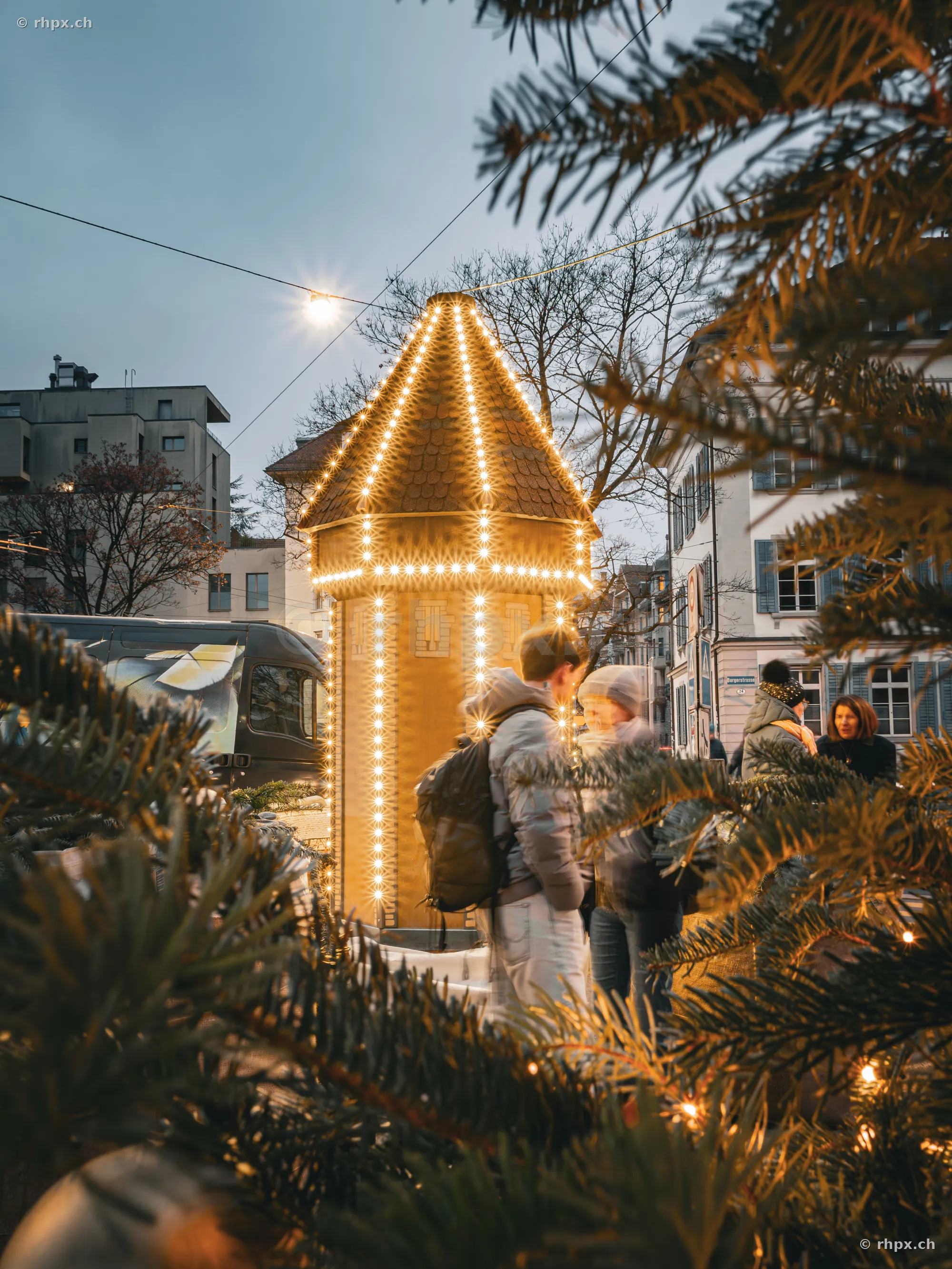 Christmas-illuminated tower in Lucerne city center with pedestrians in the foreground.
