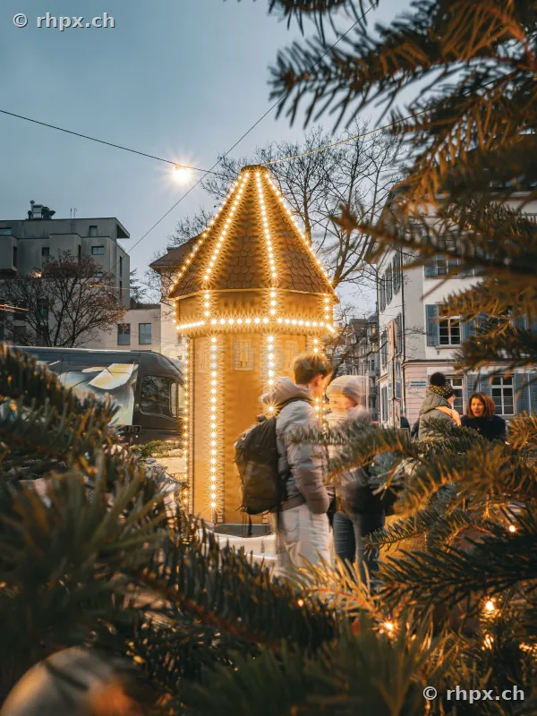 Christmas-illuminated tower in Lucerne city center with pedestrians in the foreground.