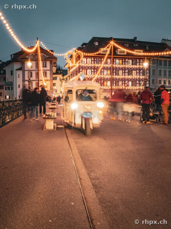 Illuminated old town street in Lucerne with a moving delivery vehicle at dusk