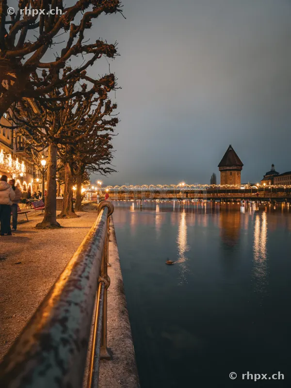 Luzerner Uferpromenade bei Nacht mit weihnachtlicher Beleuchtung und Kapellbrücke im Hintergrund.