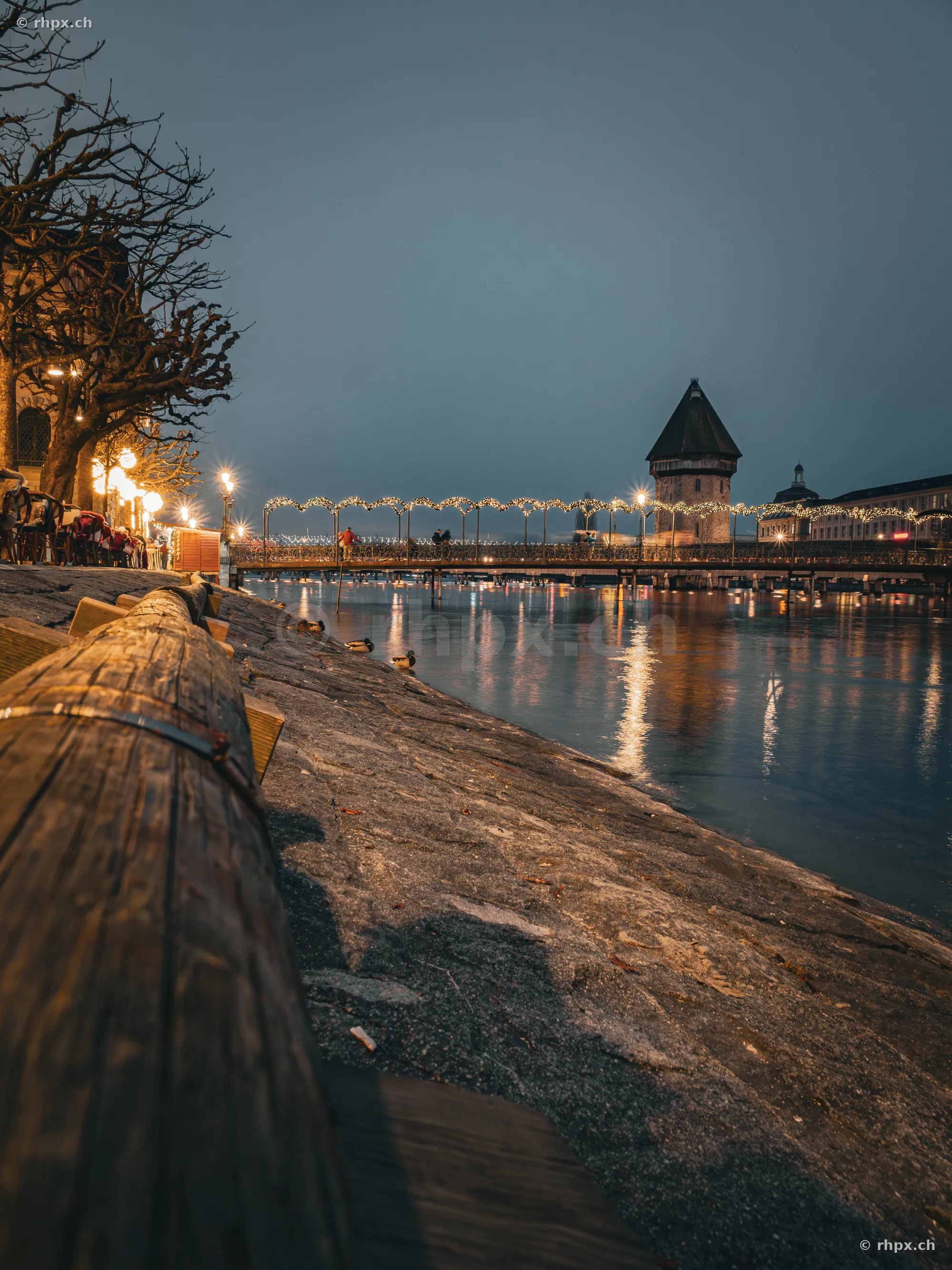 Blick entlang der Reuss in Luzern mit weihnachtlich beleuchteter Brücke und dem Wasserturm in der Dämmerung