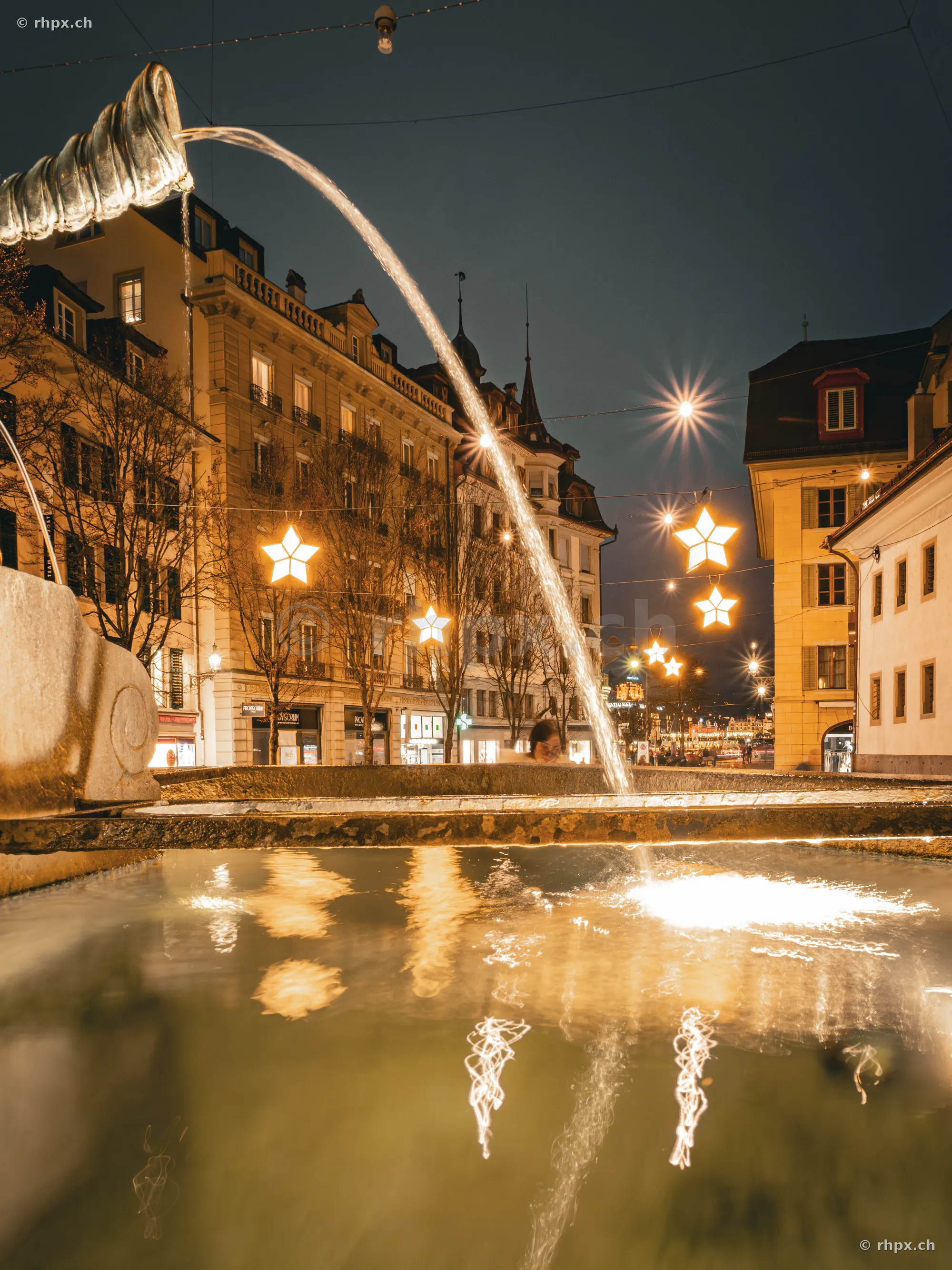 Ein Brunnen in der nächtlichen Altstadt von Luzern zur Weihnachtszeit mit leuchtenden Sternen