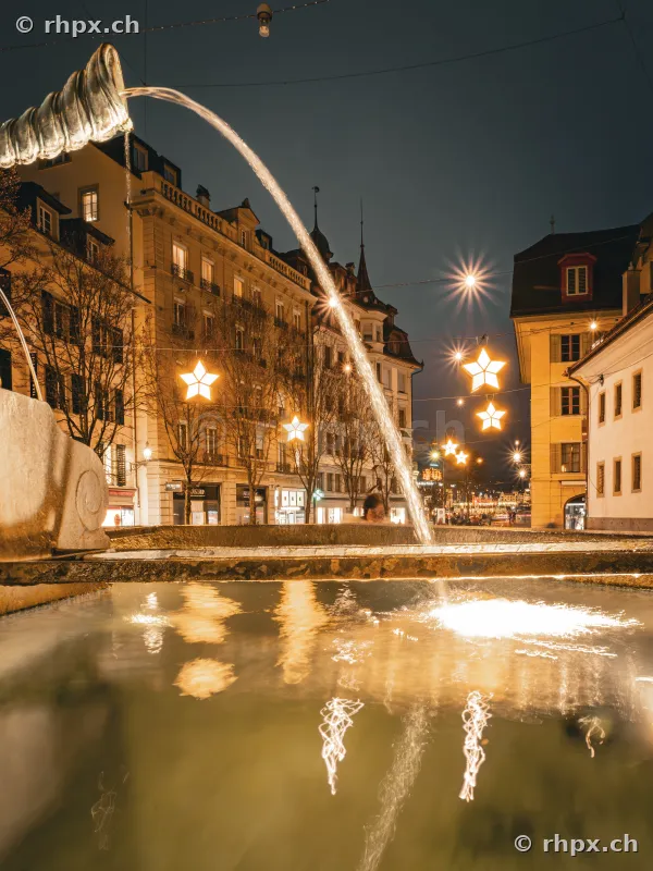 Ein Brunnen in der nächtlichen Altstadt von Luzern zur Weihnachtszeit mit leuchtenden Sternen