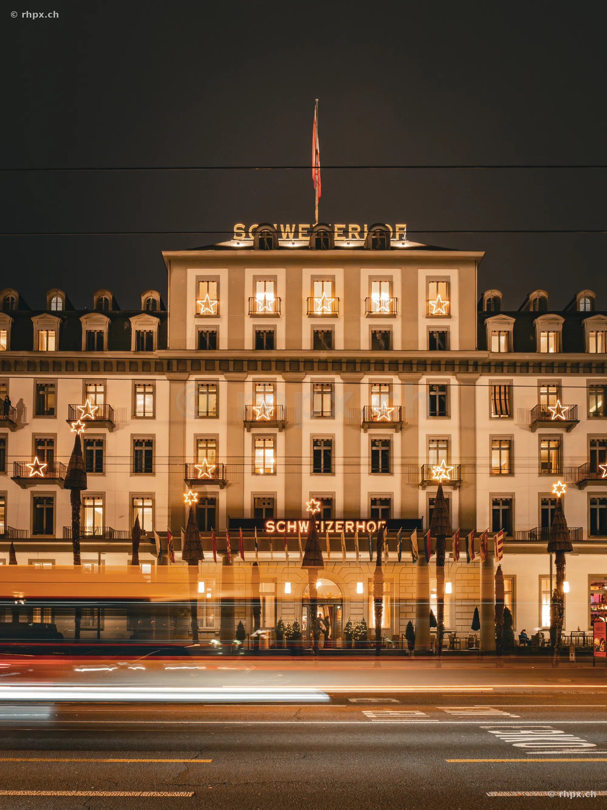 The Hotel Schweizerhof in Lucerne at night with Christmas star lighting and passing traffic