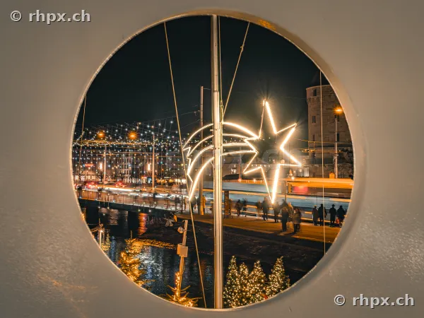 Blick durch ein rundes Fenster auf den beleuchteten Weihnachtsstern an der Reuss in Luzern.
