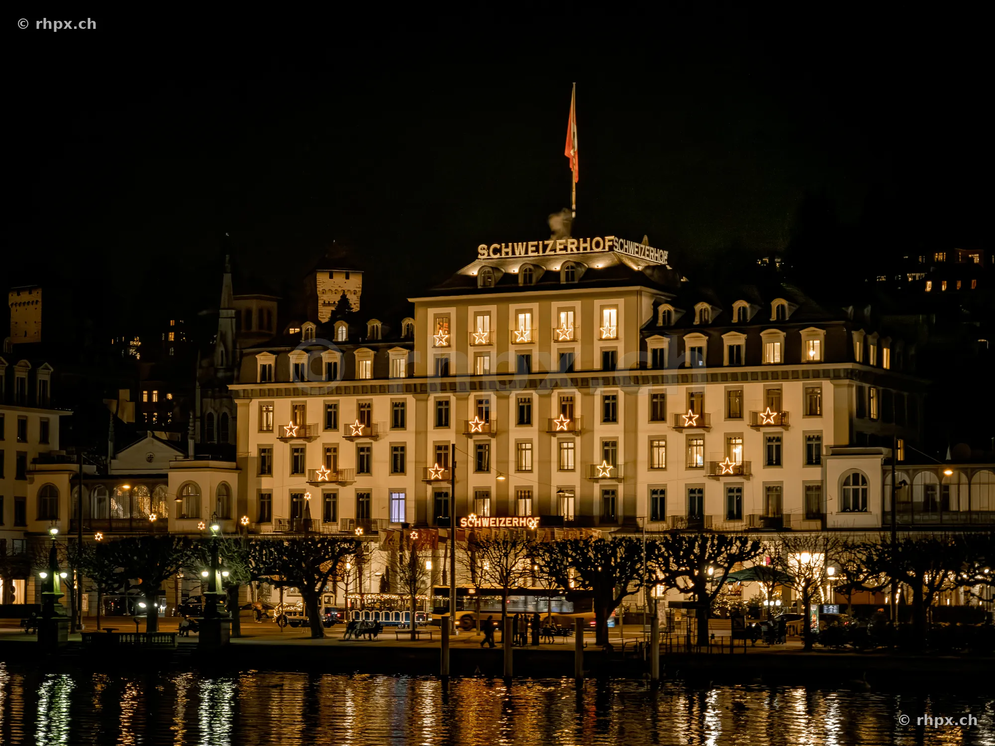 Beleuchtete Fassade des Hotels Schweizerhof in Luzern bei Dunkelheit vom See aus gesehen.