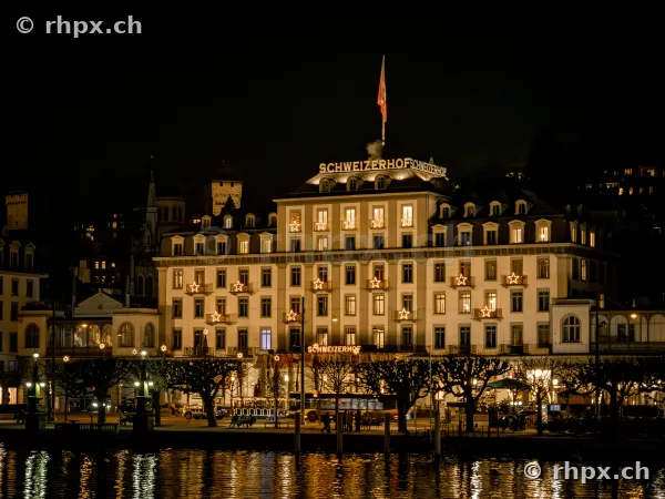 Beleuchtete Fassade des Hotels Schweizerhof in Luzern bei Dunkelheit vom See aus gesehen.
