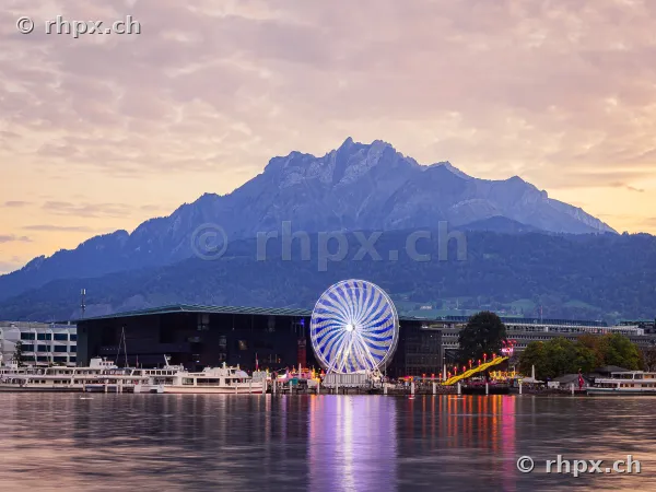 Ferris wheel of the Lozärner Määs at Lake Lucerne with Mount Pilatus in the background during twilight