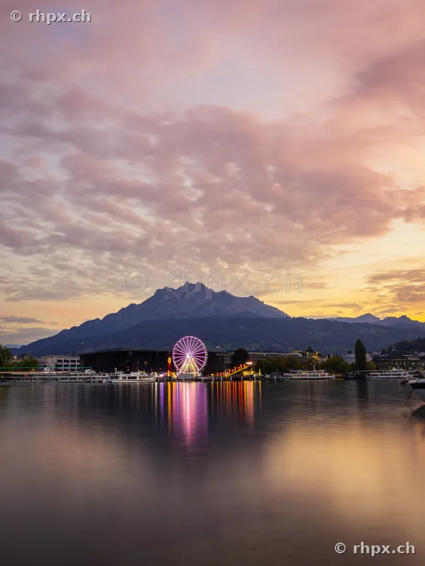 Ferris wheel of the Luzern Autumn Fair at dusk before Mount Pilatus on Lake Lucerne