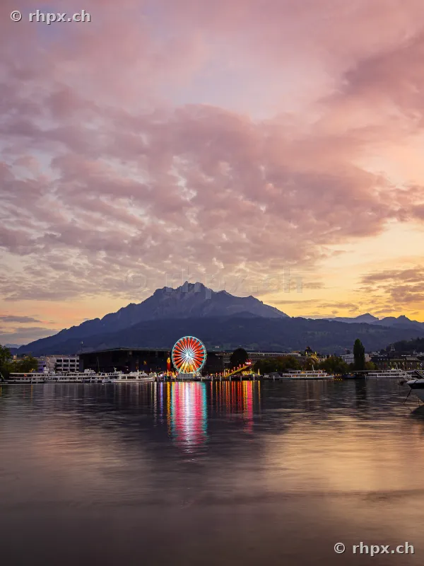 Ferris wheel at the Lozärner Määs on Lake Lucerne with Mount Pilatus in the background at dusk