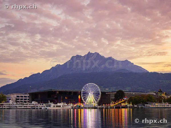 Ferris wheel at the Lucerne autumn fair during sunset at Lake Lucerne with Mount Pilatus in the background
