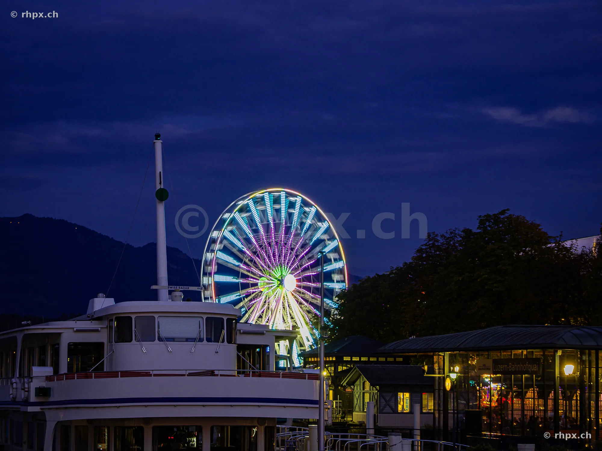 Illuminated Ferris wheel of the Lucerne Autumn Fair at night in front of a passenger ship