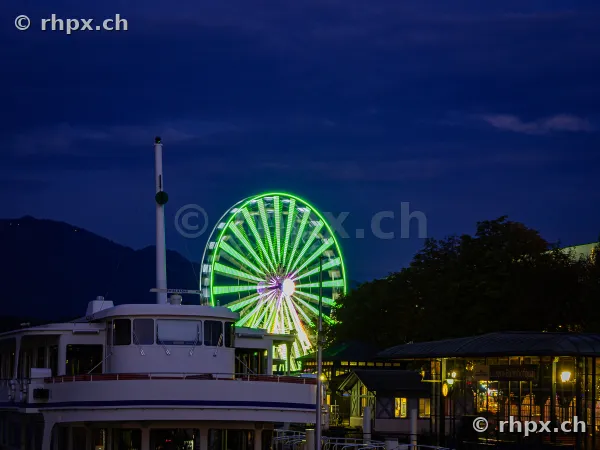 Ferris wheel of the Lucerne Autumn Fair by the lake at night with a ship in the foreground