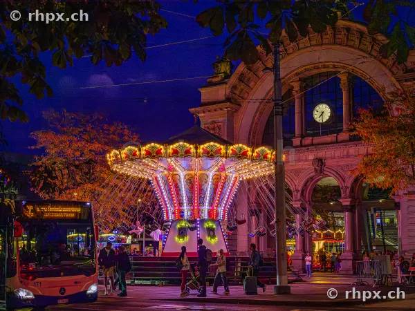 Chain carousel at the Lozärner Määs in front of the historic railway station portal at night