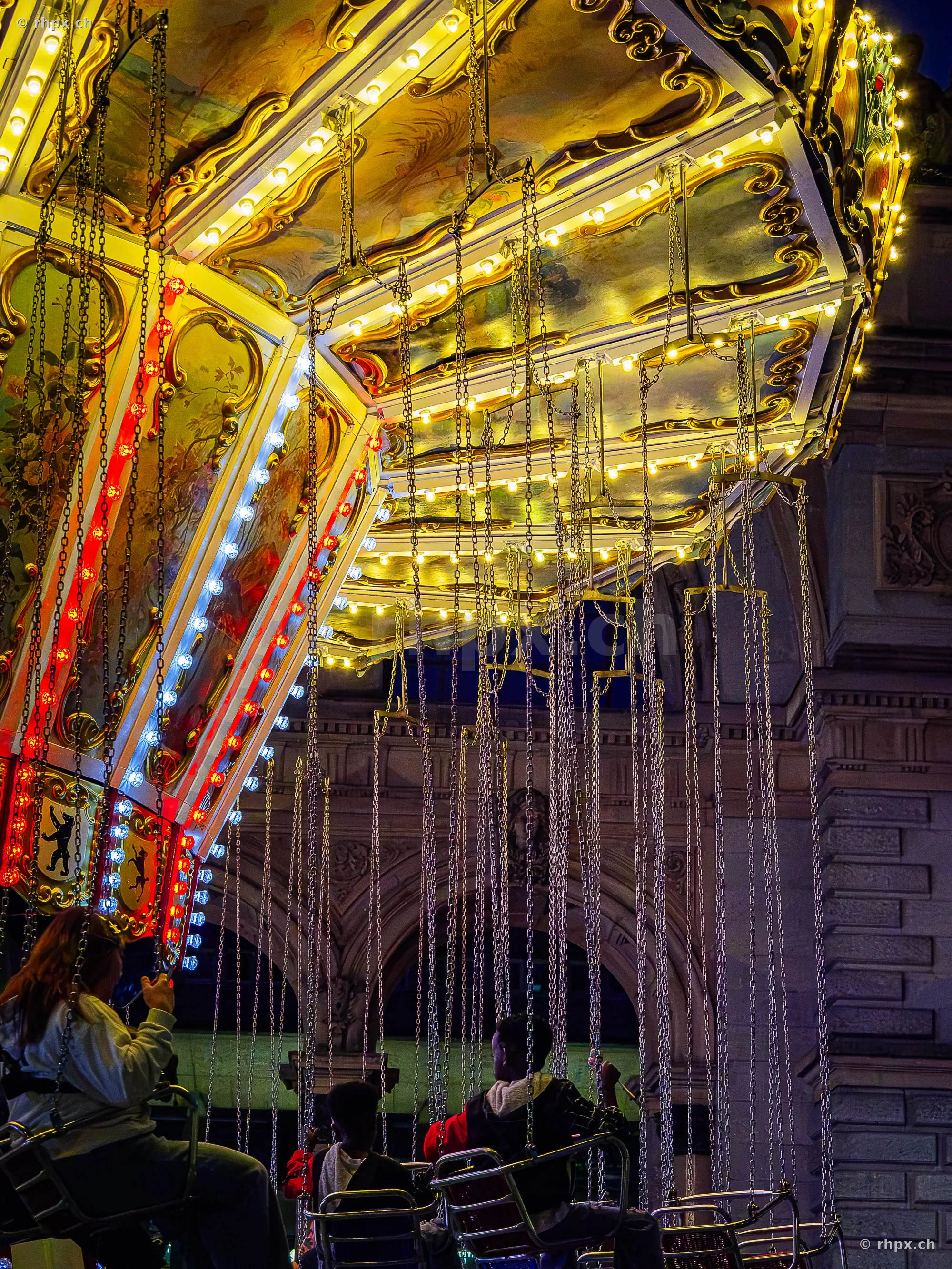 Illuminated chain carousel with people at the Lucerne Määs at night