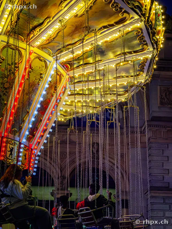 Illuminated chain carousel with people at the Lucerne Määs at night