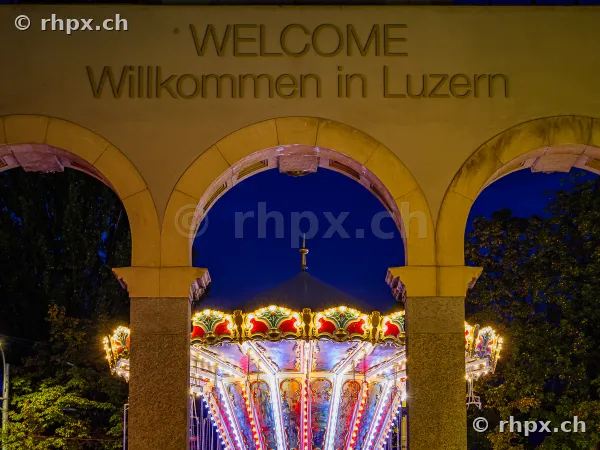 The illuminated carousel of the Lucerne Autumn Fair under the archway