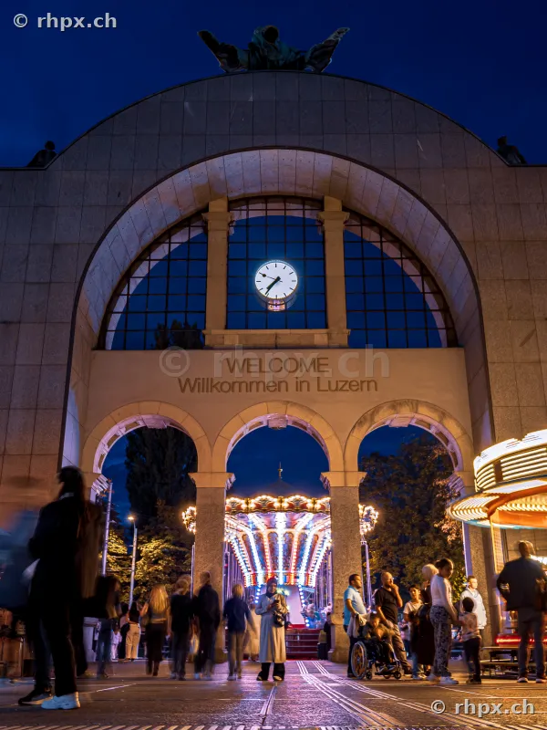 Lucerne station gate in the evening with a view of an illuminated fairground carousel.