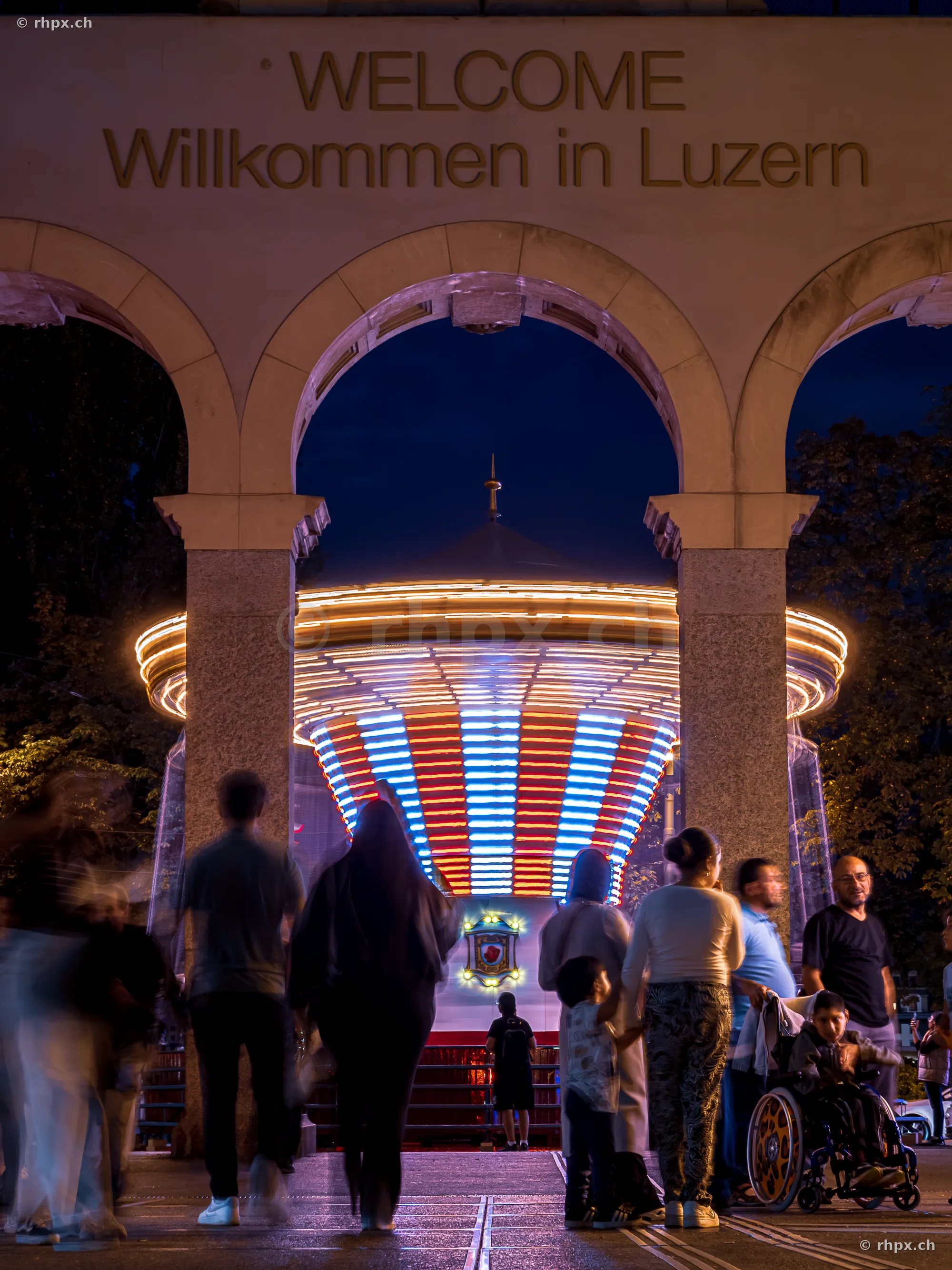 Welcome arch of the Lucerne Autumn Fair with illuminated carousel in the background