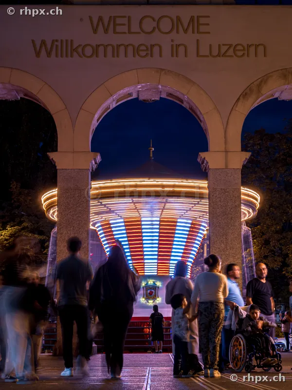 Welcome arch of the Lucerne Autumn Fair with illuminated carousel in the background