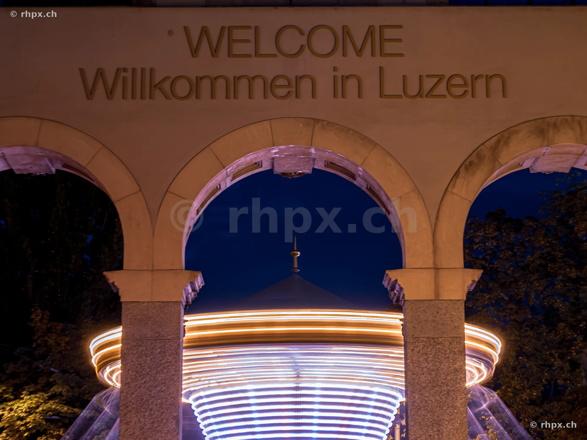 View through a stone archway at a glowing carousel at the Luzerner Määs autumn fair at night