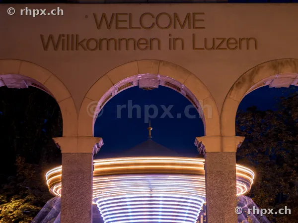 View through a stone archway at a glowing carousel at the Luzerner Määs autumn fair at night