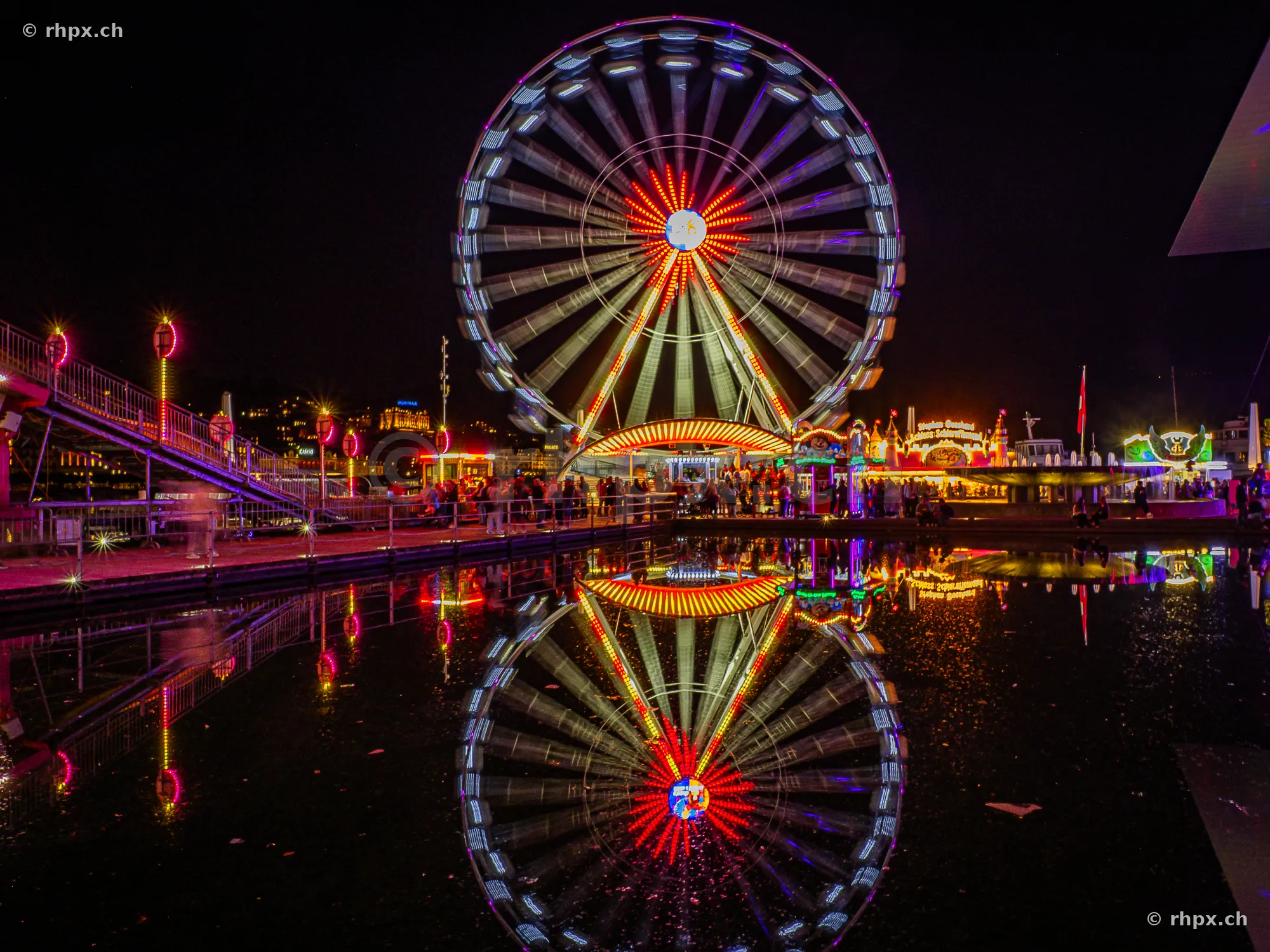 Illuminated Ferris wheel at the Lucerne Autumn Fair at night reflected in the water.