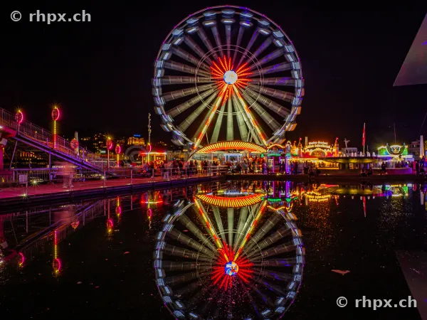 Illuminated Ferris wheel at the Lucerne Autumn Fair at night reflected in the water.