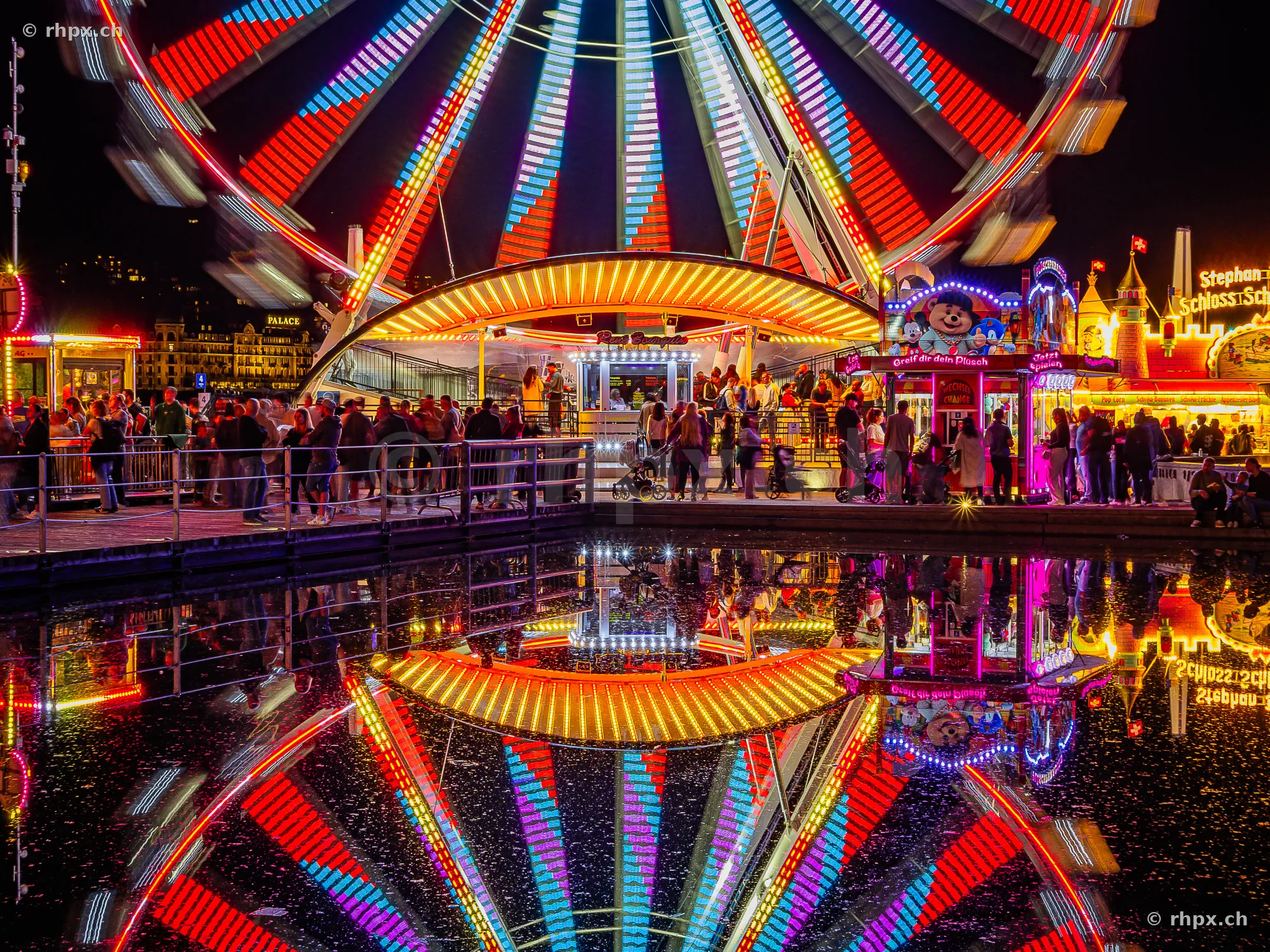 Ferris wheel and fairground stalls at the Lucerne autumn fair at night with reflection in water