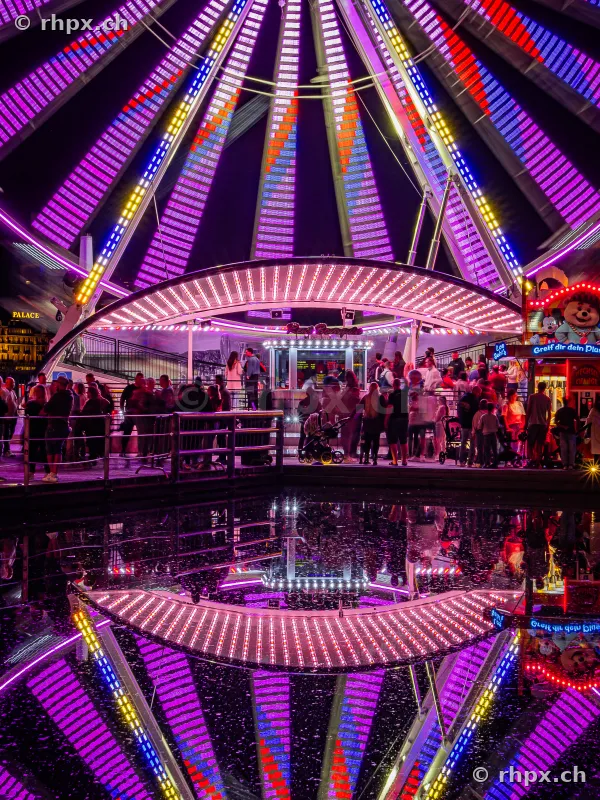 Ferris wheel at the Lucerne Määs at night with light reflection in the water.