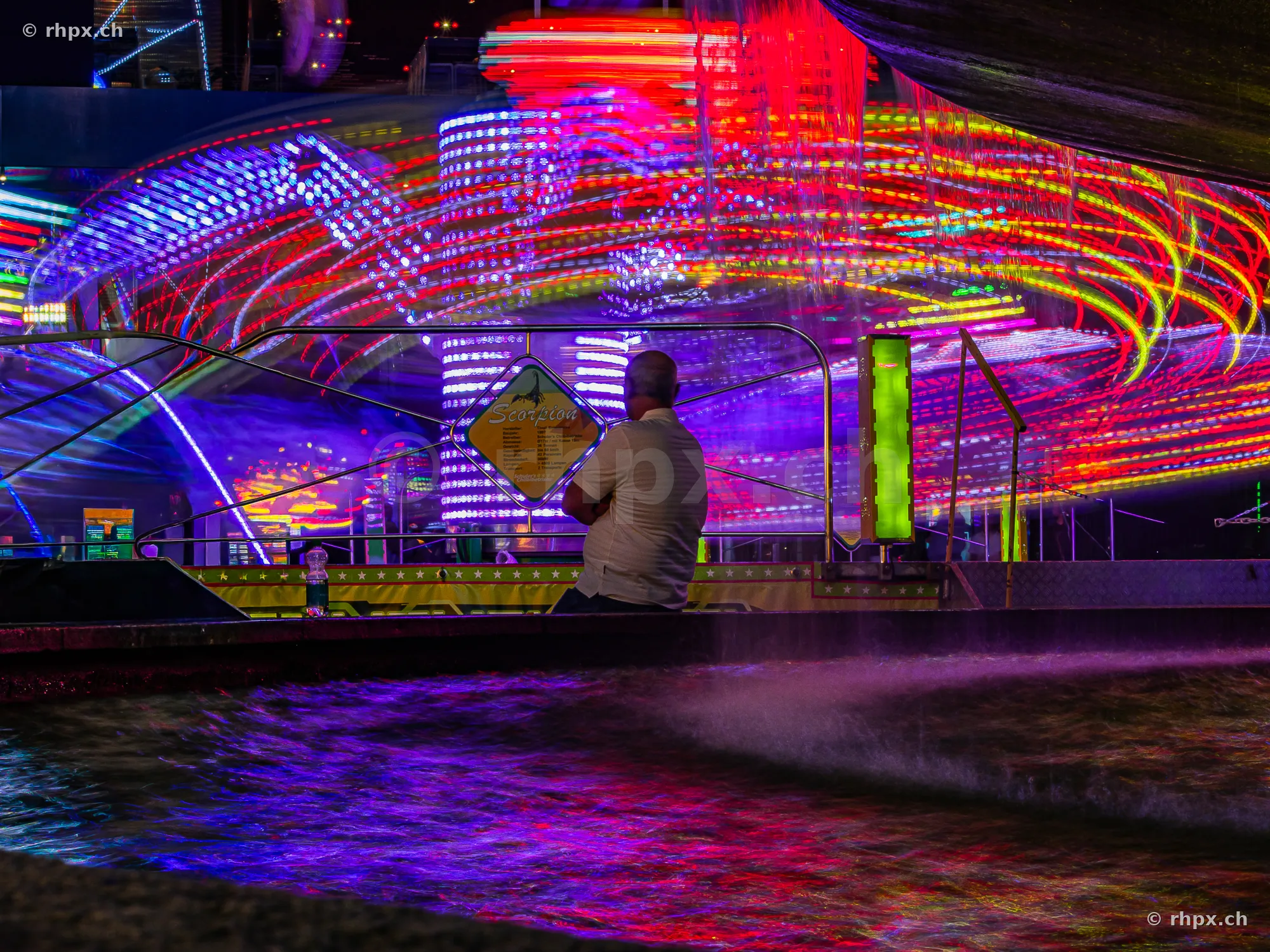 Observer in front of a glowing amusement ride at the Lucerne Autumn Fair at night