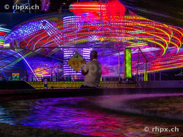 Observer in front of a glowing amusement ride at the Lucerne Autumn Fair at night