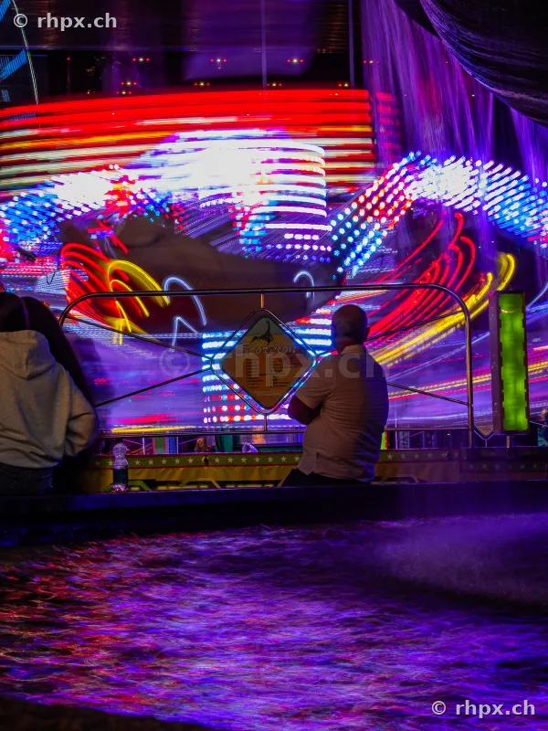 People watching a brightly lit carousel at night at the Lucerne Fair.
