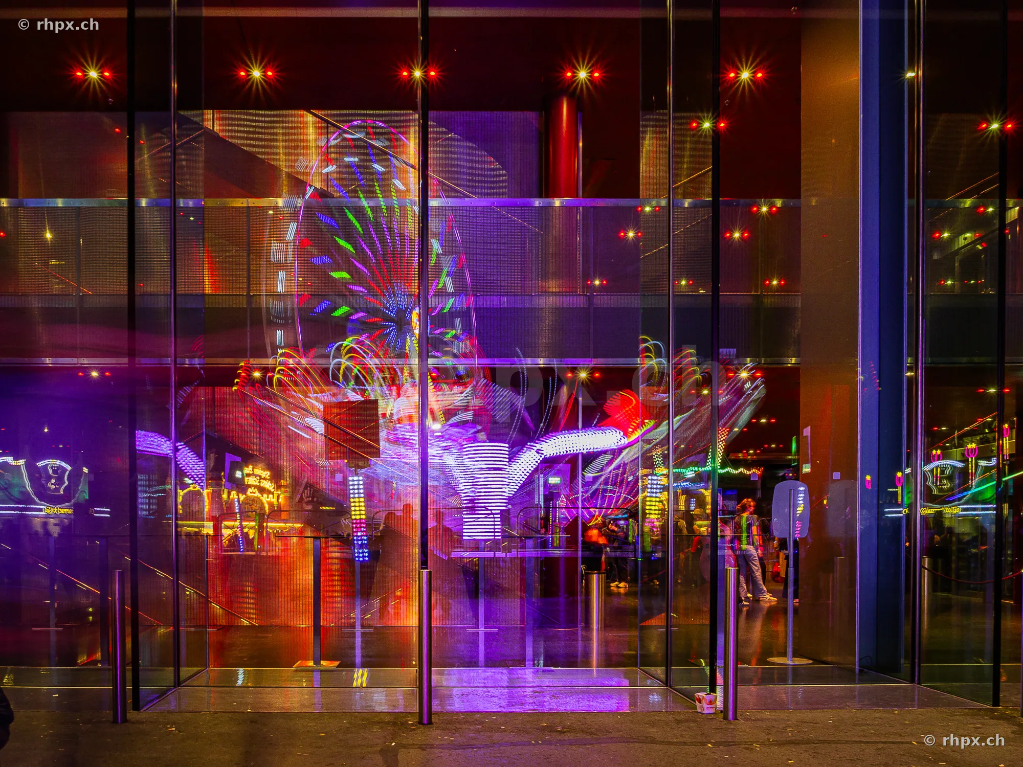 Reflection of lights and fairground rides of the Lucerne Autumn Fair in a modern glass front.