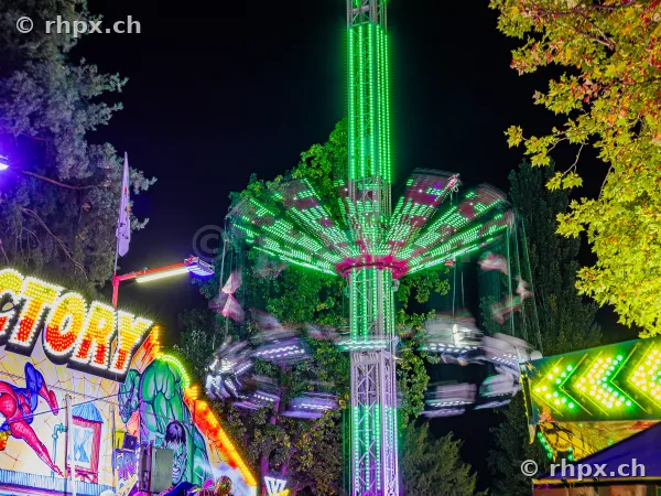 Chain swing ride with a green illuminated tower at night at the Lucerne autumn fair