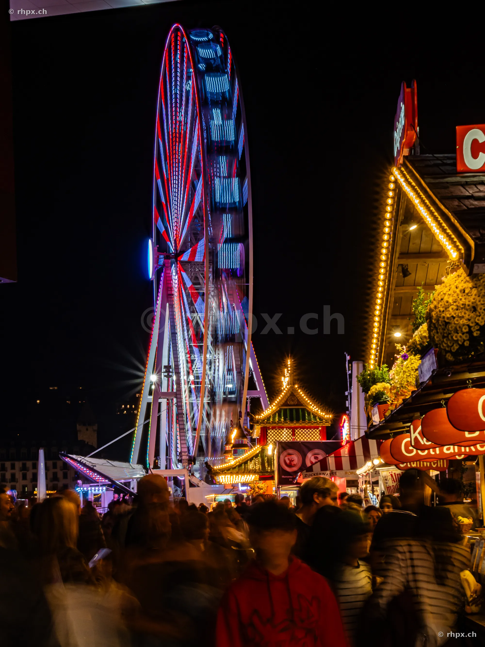 Beleuchtetes Riesenrad auf der Luzerner Herbstmesse bei Nacht mit Besuchern