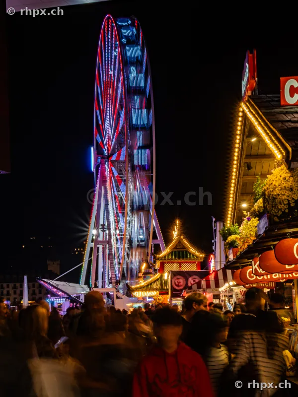 Illuminated Ferris wheel at the Lucerne Autumn Fair at night with visitors